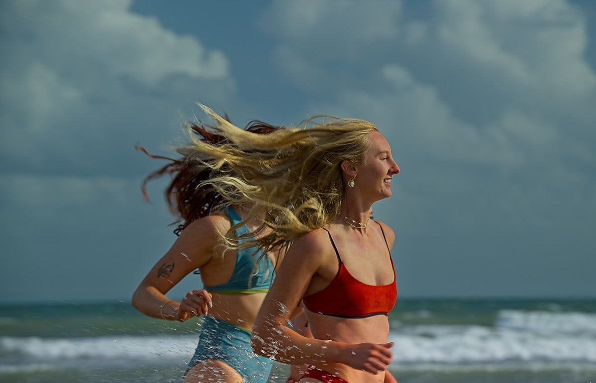 Two women running on a beach with ocean and sky in the background