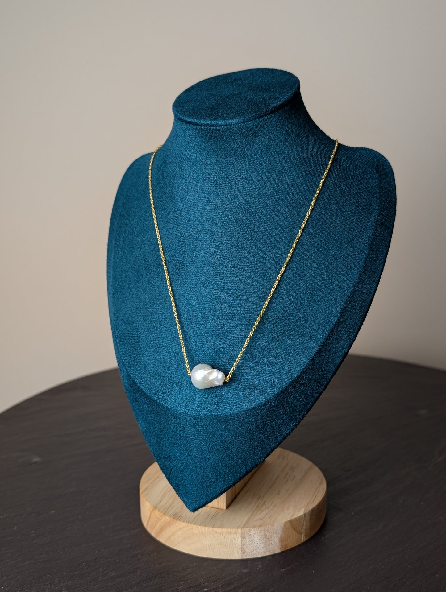 Nacre Necklace by Nudie – studio photo showing the baroque freshwater pearl pendant resting on a green and wooden mannequin, with delicate hammered gold chain.