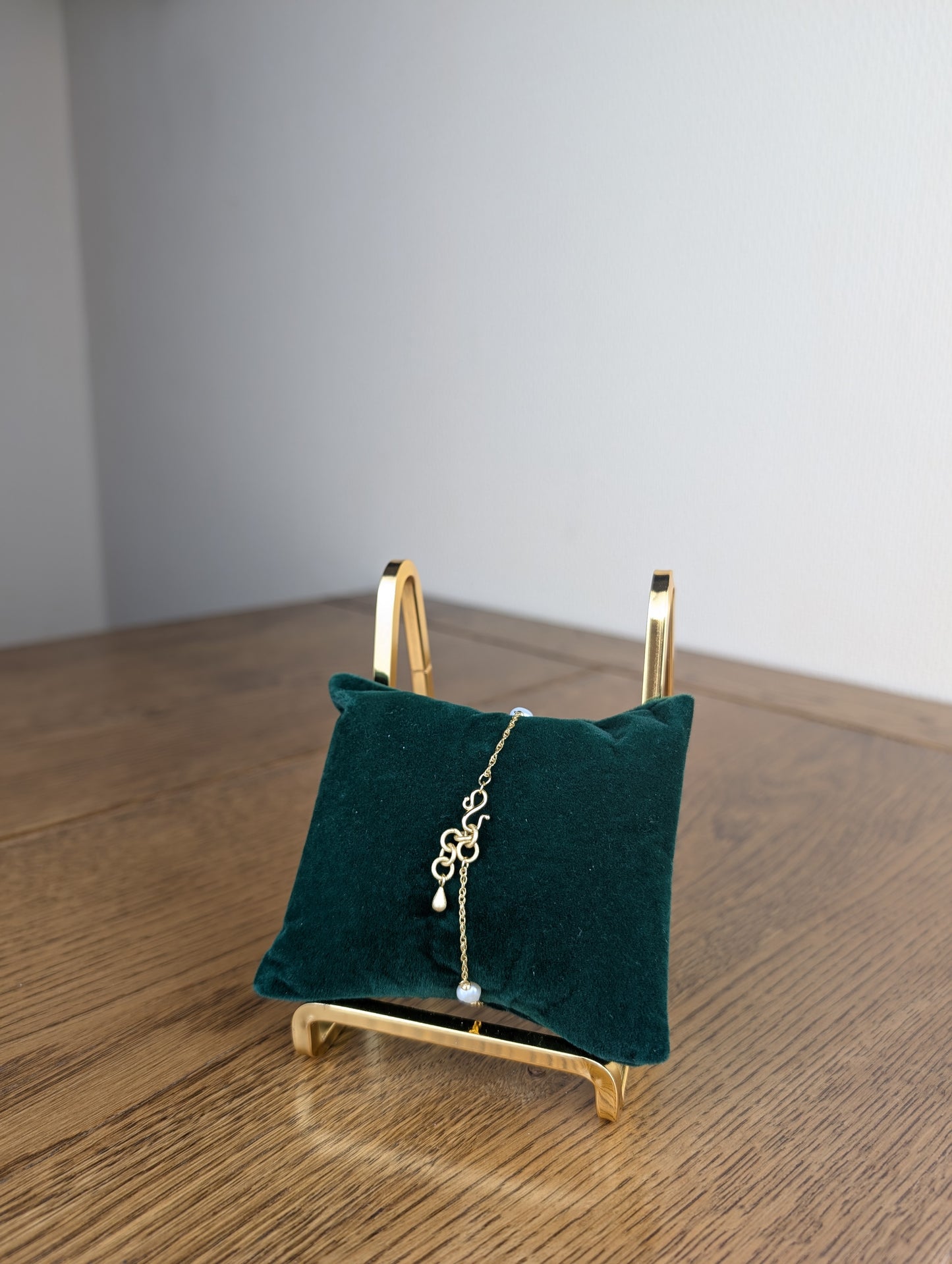 Gold bracelet on a green pillow with a gold stand against a gray wall.