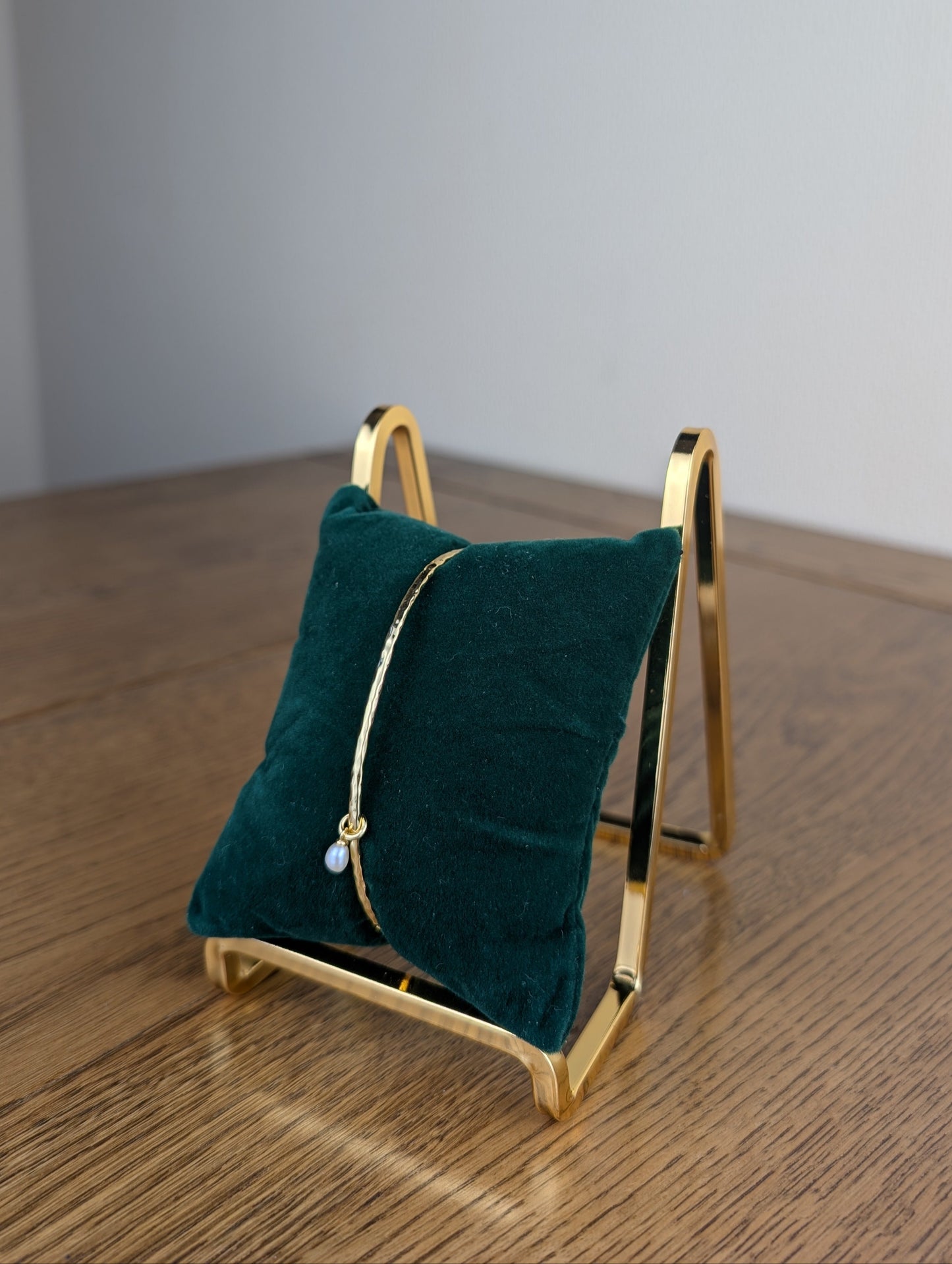 Gold jewelry stand with a green cushion holding a piece of jewelry on a wooden surface.