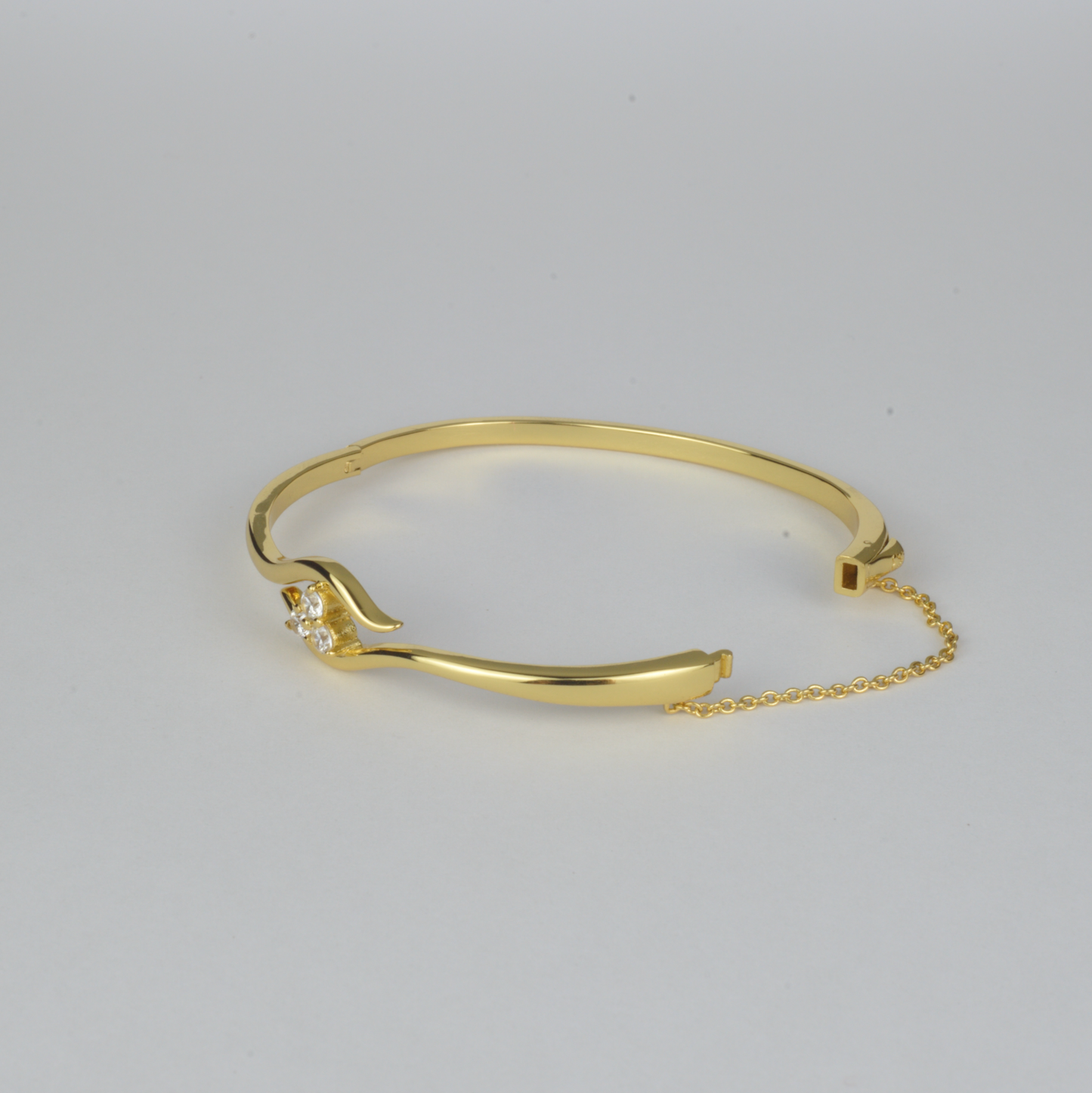 Avalon Bangle by Nudie – studio photo on white background showing the bangle laid flat with open clasp and visible safety chain, highlighting textured gold and crystal detail.