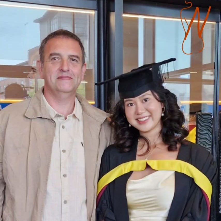 Graduate in cap and gown standing next to an adult, with a blurred background