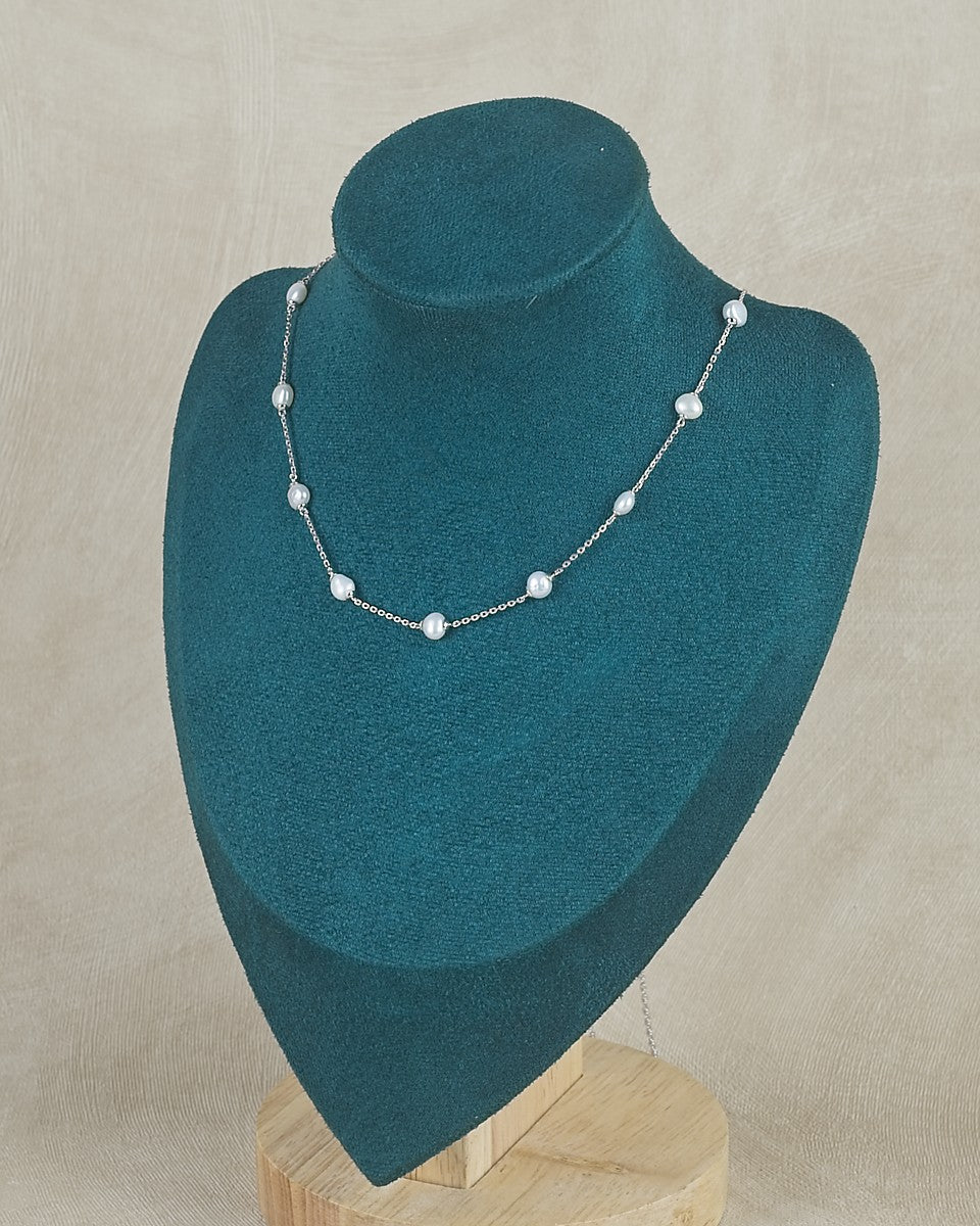 Pearl necklace on a teal mannequin bust against a beige background
