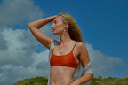 Woman in an orange sports bra and gray cover-up against a blue sky with clouds