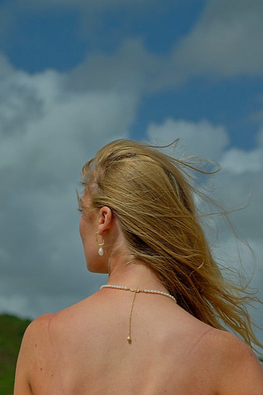 Woman in a red bikini top and white cover-up standing on a beach with a blue sky and clouds in the background.