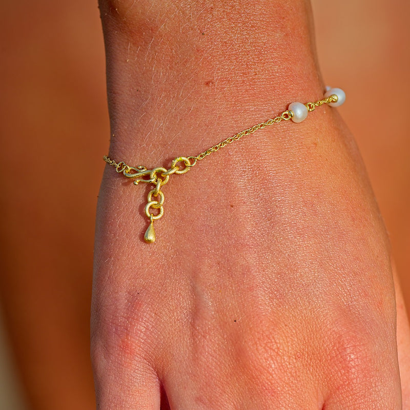 Gold anklet with a pearl charm on a person's ankle against a blurred background