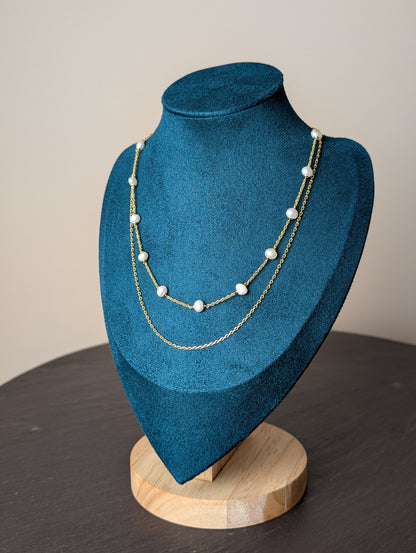 Maris Necklace by Nudie – studio photo showing freshwater pearls on a fine gold chain, layered with a second twisted strand, displayed on a green and wooden mannequin.