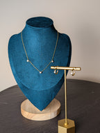 Avalon Duo Set by Nudie – studio photo with necklace hanging on green and wooden mannequin and matching earring displayed on a gold stand atop a slate table.