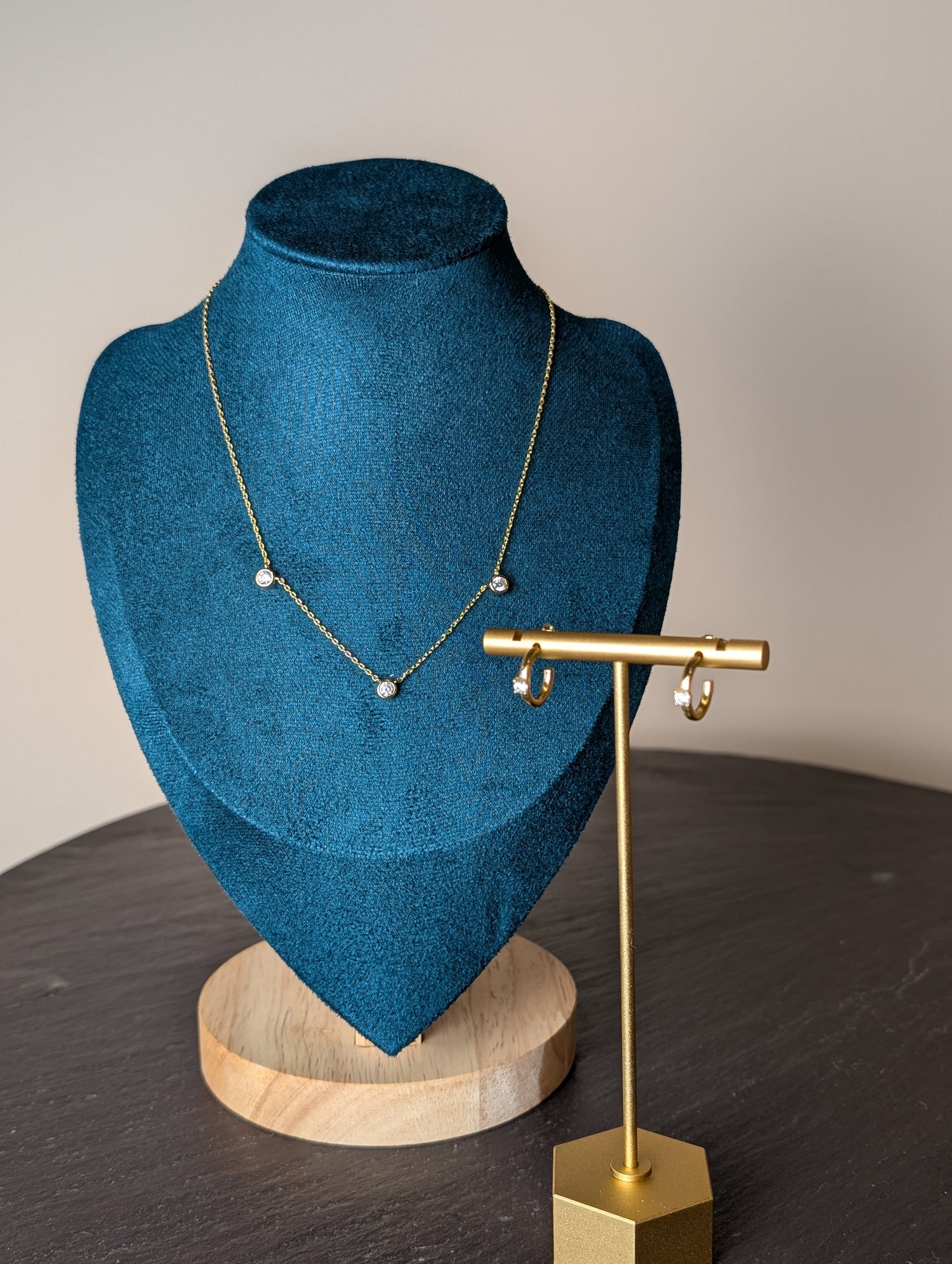 Avalon Duo Set by Nudie – studio photo with necklace hanging on green and wooden mannequin and matching earring displayed on a gold stand atop a slate table.