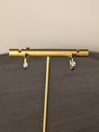 Avalon Earrings by Nudie – close-up studio photo showing hammered gold hoops on a gold earring stand, with a softly blurred background and slate table beneath.