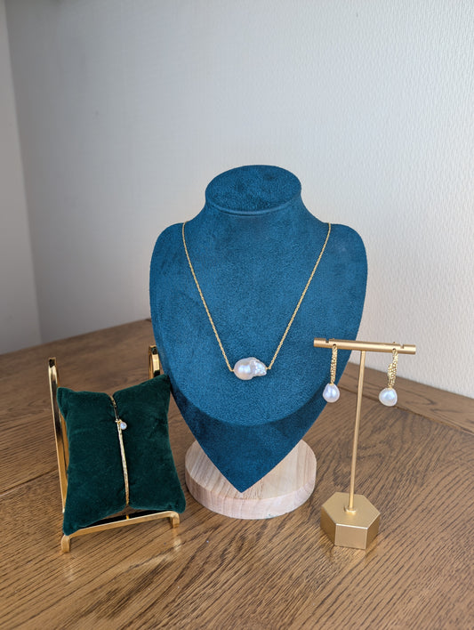 Jewelry display with necklace on blue velvet bust, earrings on gold stand, and green jewelry box on wooden surface.