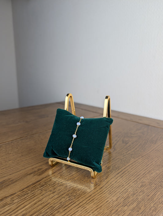 Gold jewelry stand with a green cushion holding a necklace on a wooden surface.