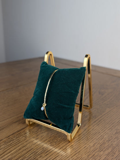 Gold jewelry stand with a green cushion holding a piece of jewelry on a wooden surface.