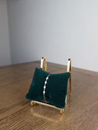 Green velvet jewelry display with a gold stand on a wooden surface