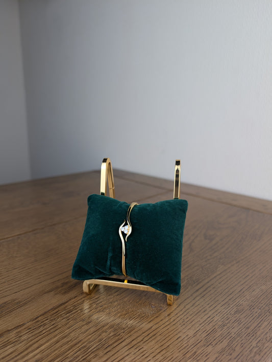 Green velvet jewelry stand with a gold base on a wooden surface.