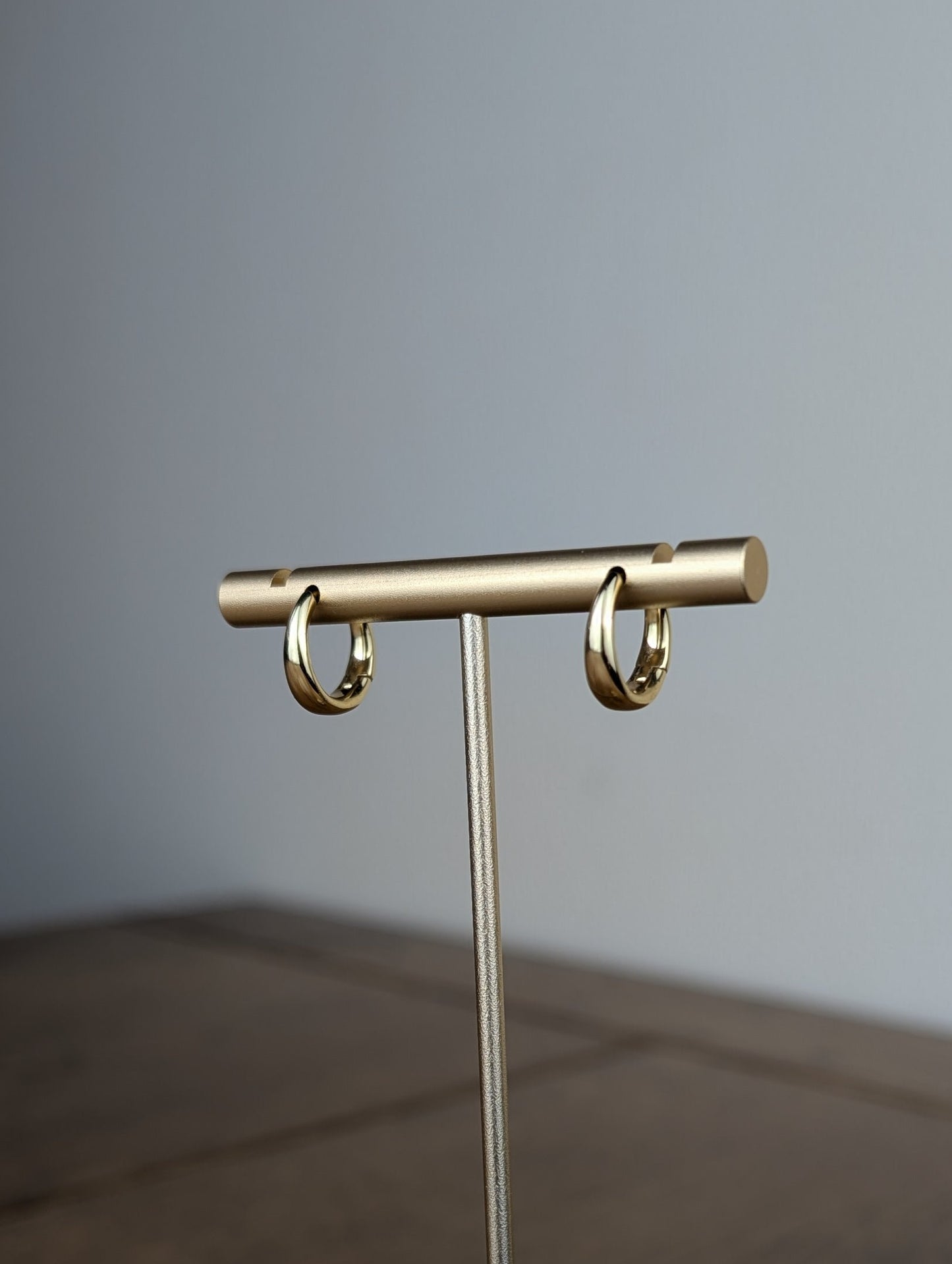 Gold jewelry stand on a wooden surface with a gray background