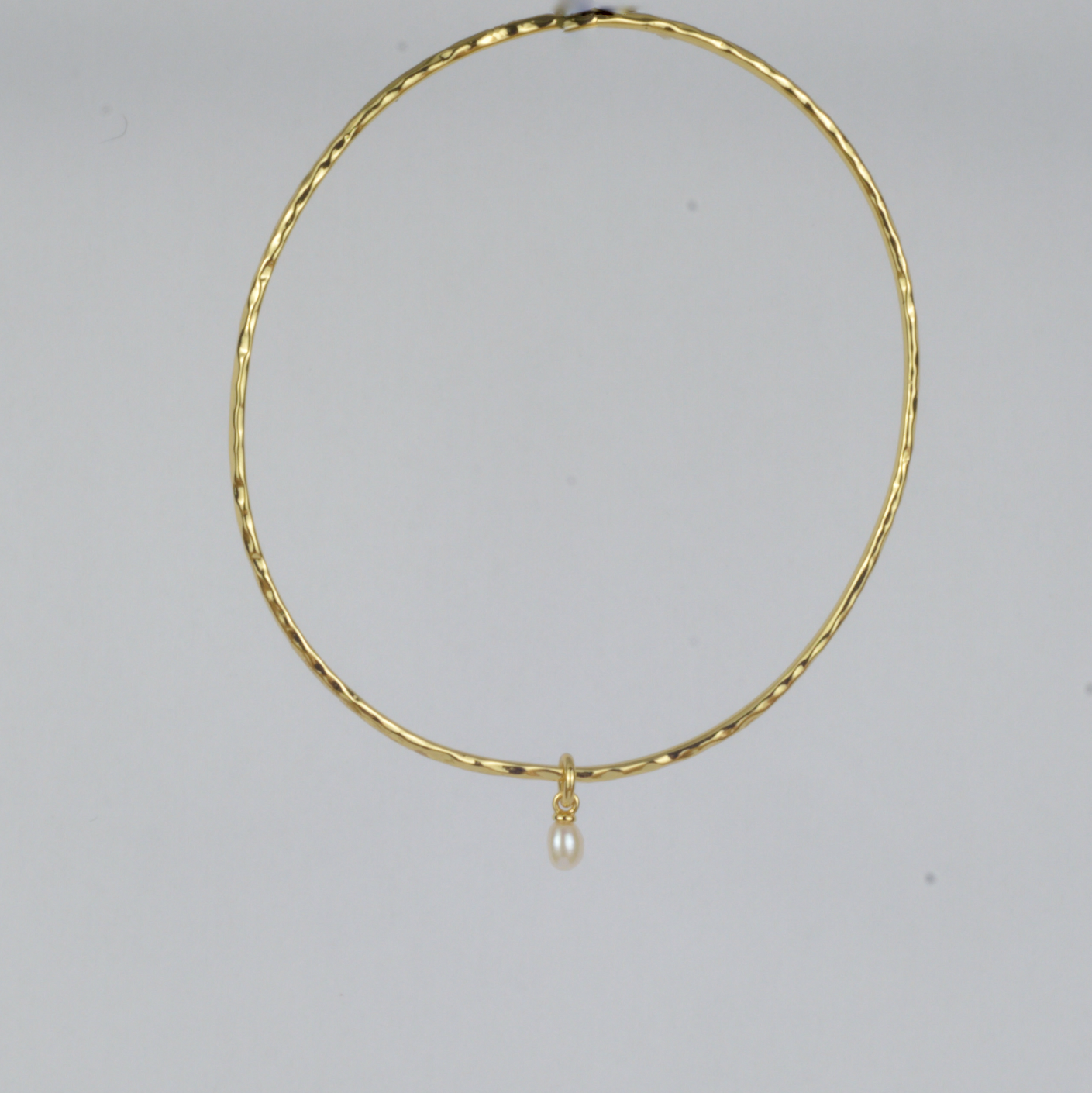 Nacre Bangle by Nudie – studio photo on white background showing the bangle hanging front-on to the camera, highlighting its sculpted shape and pearl detail.