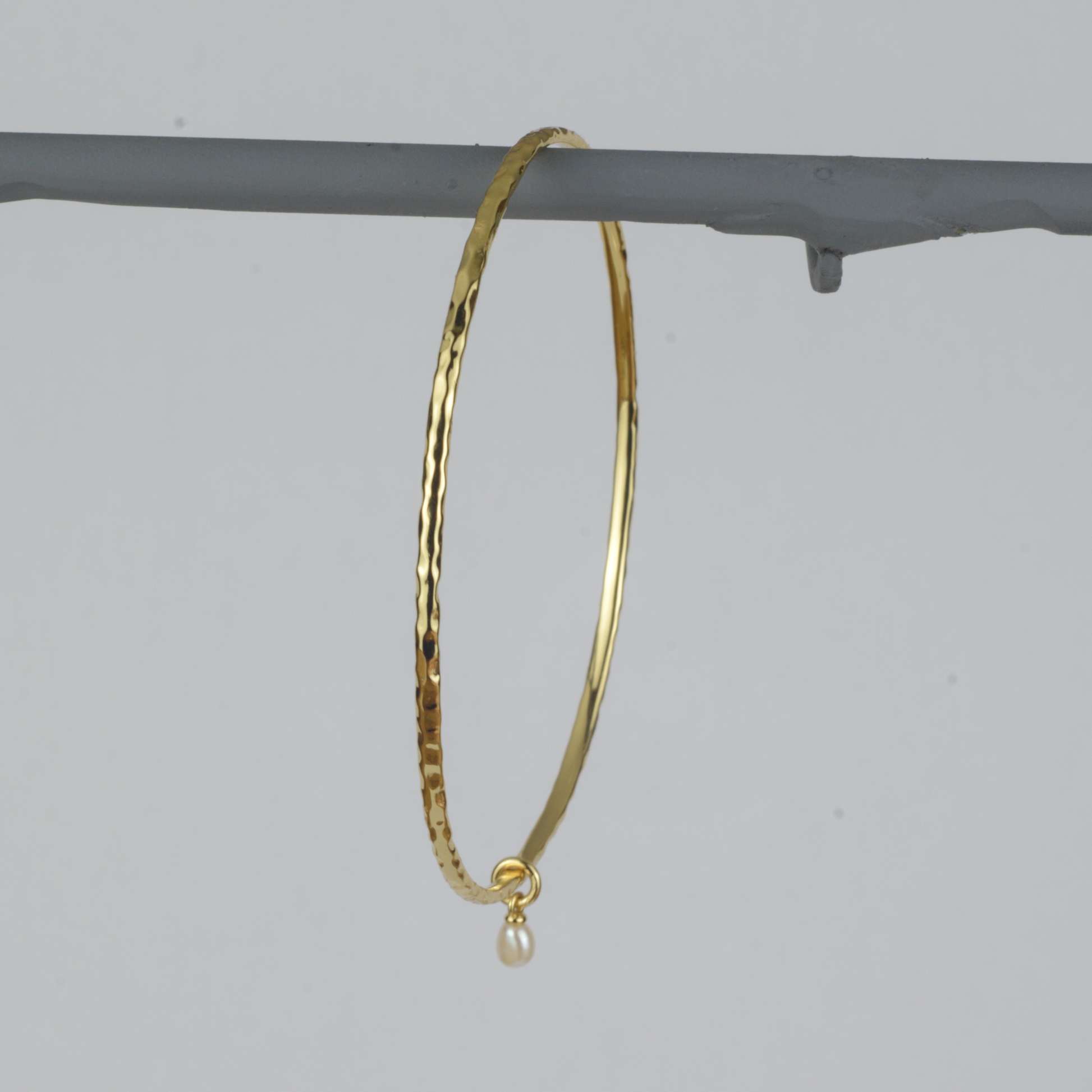 Nacre Bangle by Nudie – studio photo on white background showing the sculpted open bangle hanging upright, with a hammered 18k gold-plated finish.