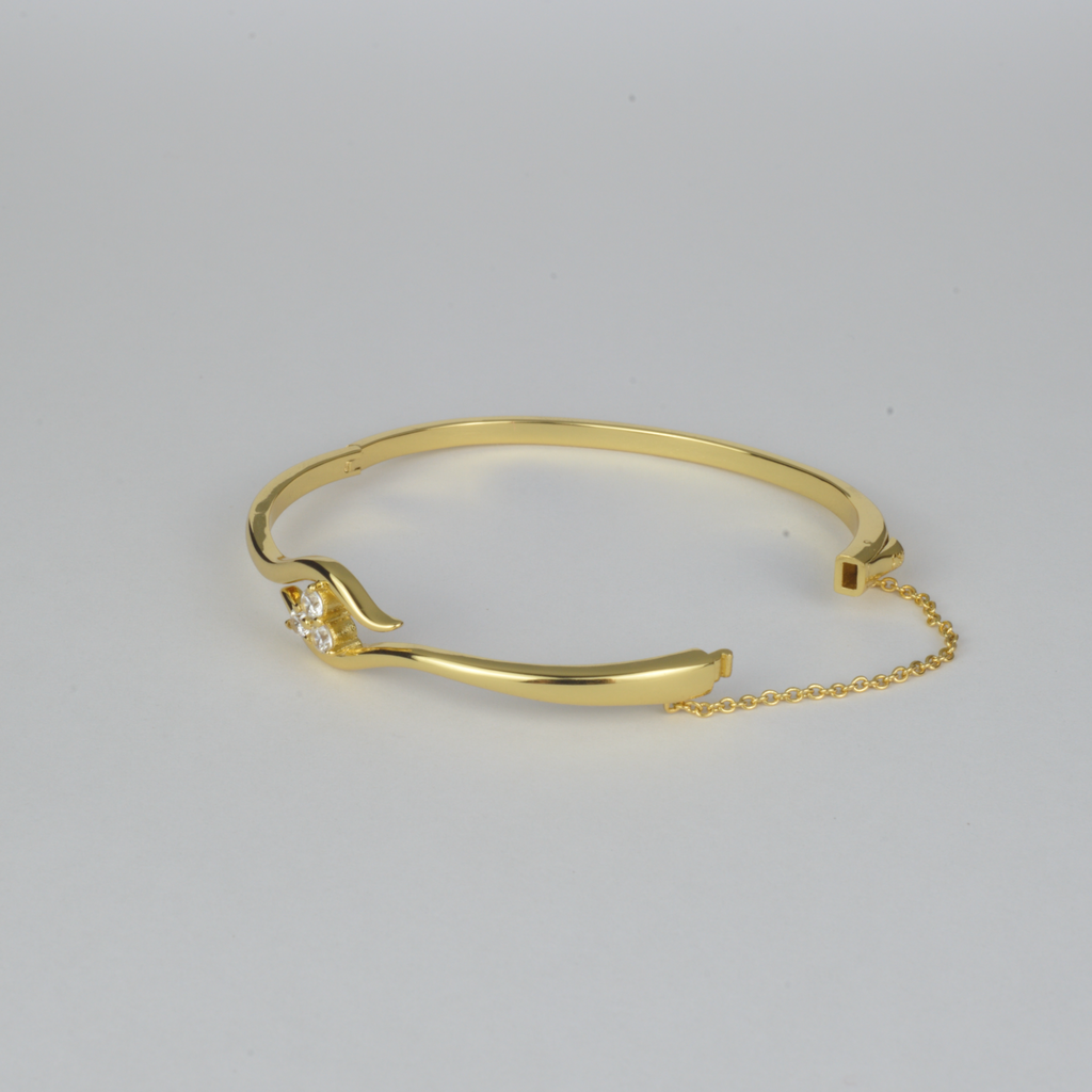 Avalon Bangle by Nudie – studio photo on white background showing the bangle laid flat with open clasp and visible safety chain, highlighting textured gold and crystal detail.