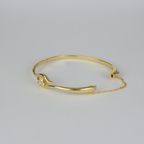 Avalon Bangle by Nudie – studio photo on white background showing the bangle laid flat with open clasp and visible safety chain, highlighting textured gold and crystal detail.