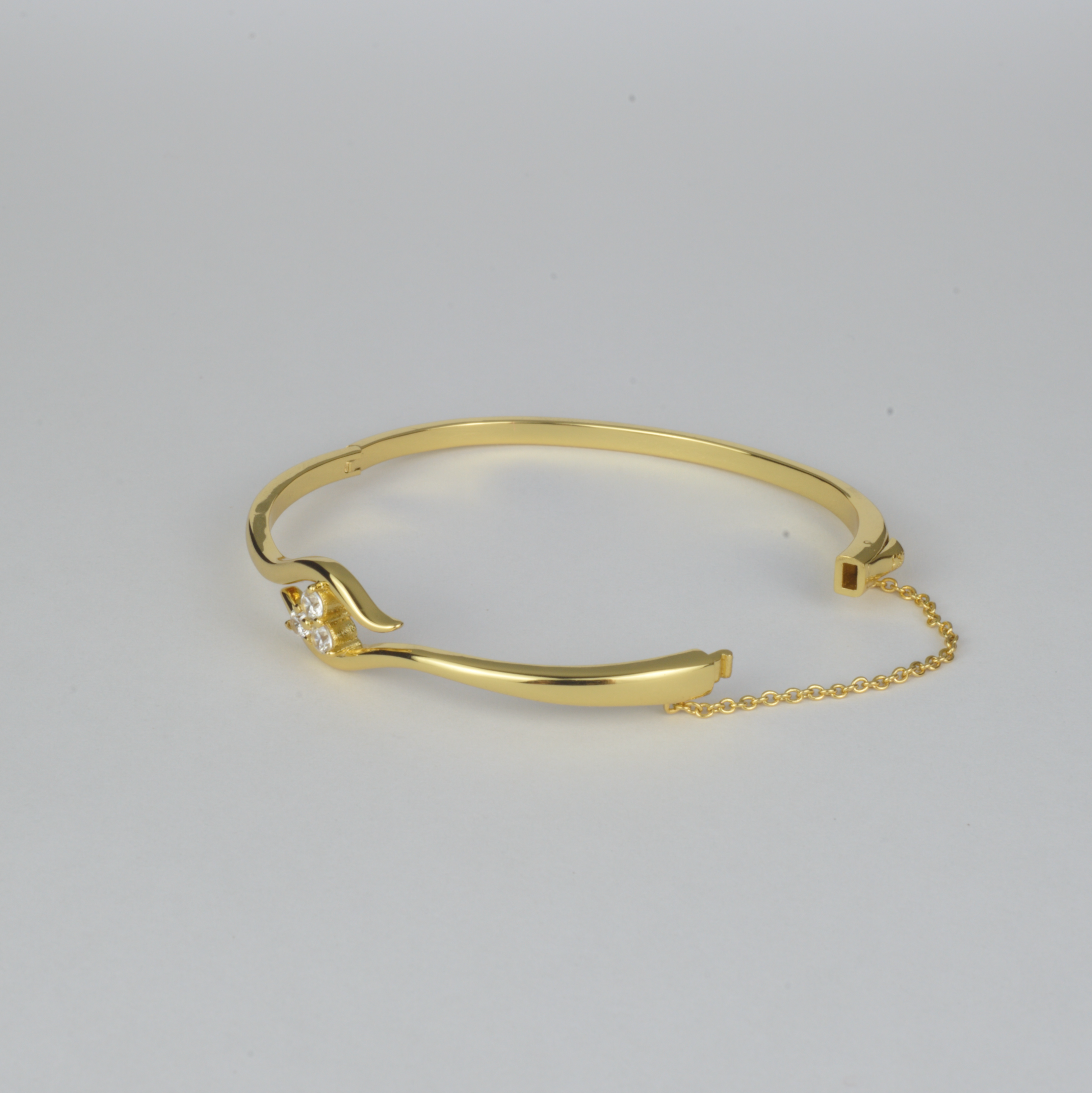Avalon Bangle by Nudie – studio photo on white background showing the bangle laid flat with open clasp and visible safety chain, highlighting textured gold and crystal detail.