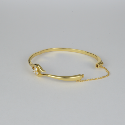 Avalon Bangle by Nudie – studio photo on white background showing the bangle laid flat with open clasp and visible safety chain, highlighting textured gold and crystal detail.
