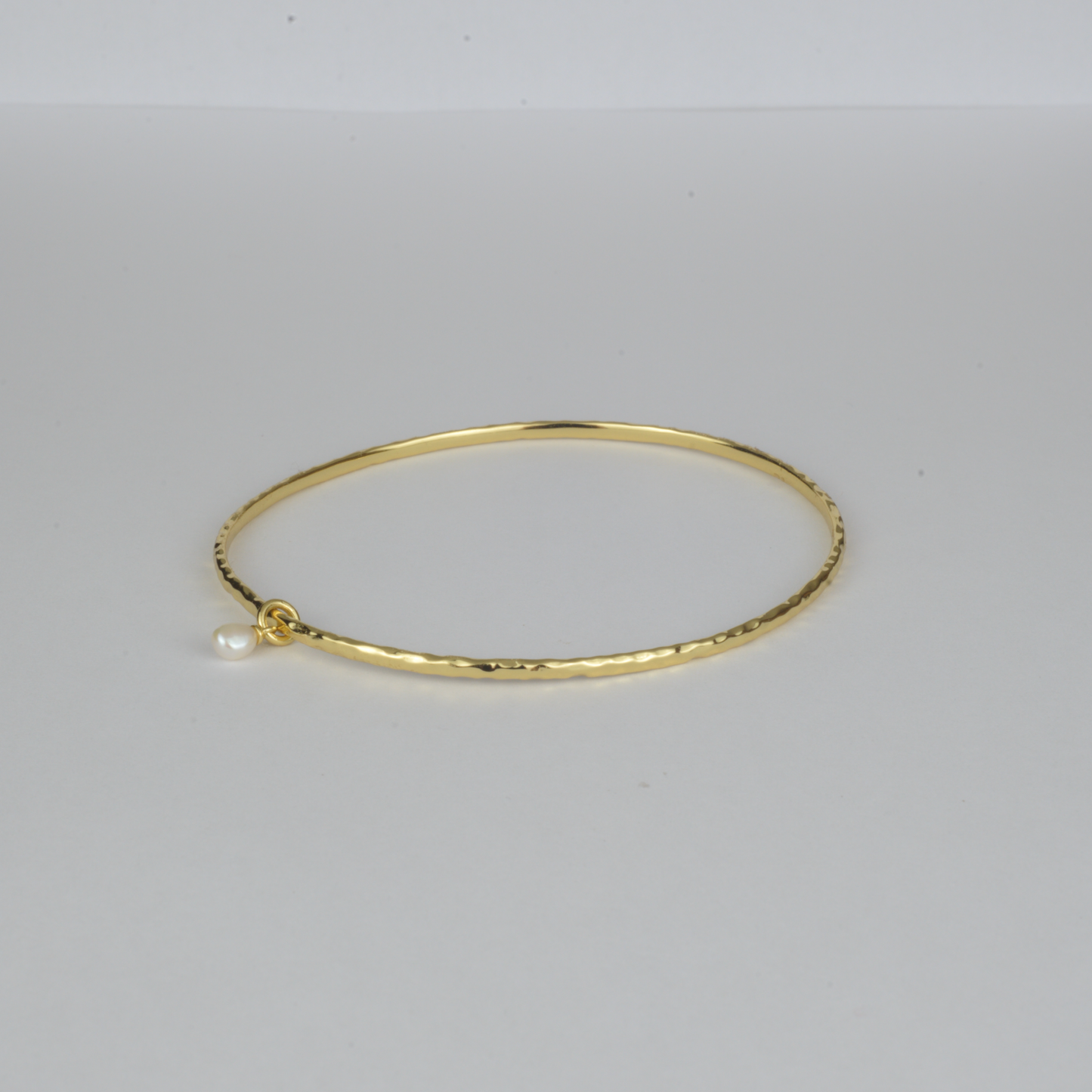 Nacre Bangle by Nudie – studio photo on white background showing the open bangle laid flat, featuring a petite freshwater pearl and hammered gold finish.