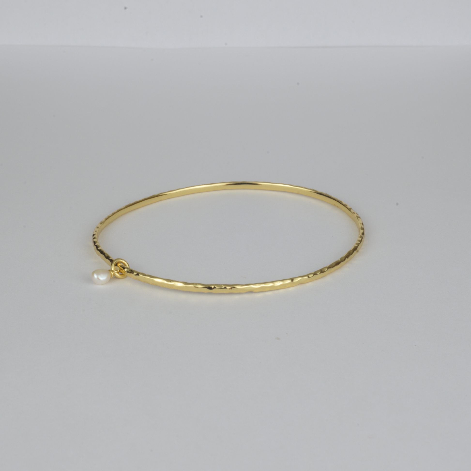 Nacre Bangle by Nudie – studio photo on white background showing the open bangle laid flat, featuring a petite freshwater pearl and hammered gold finish.