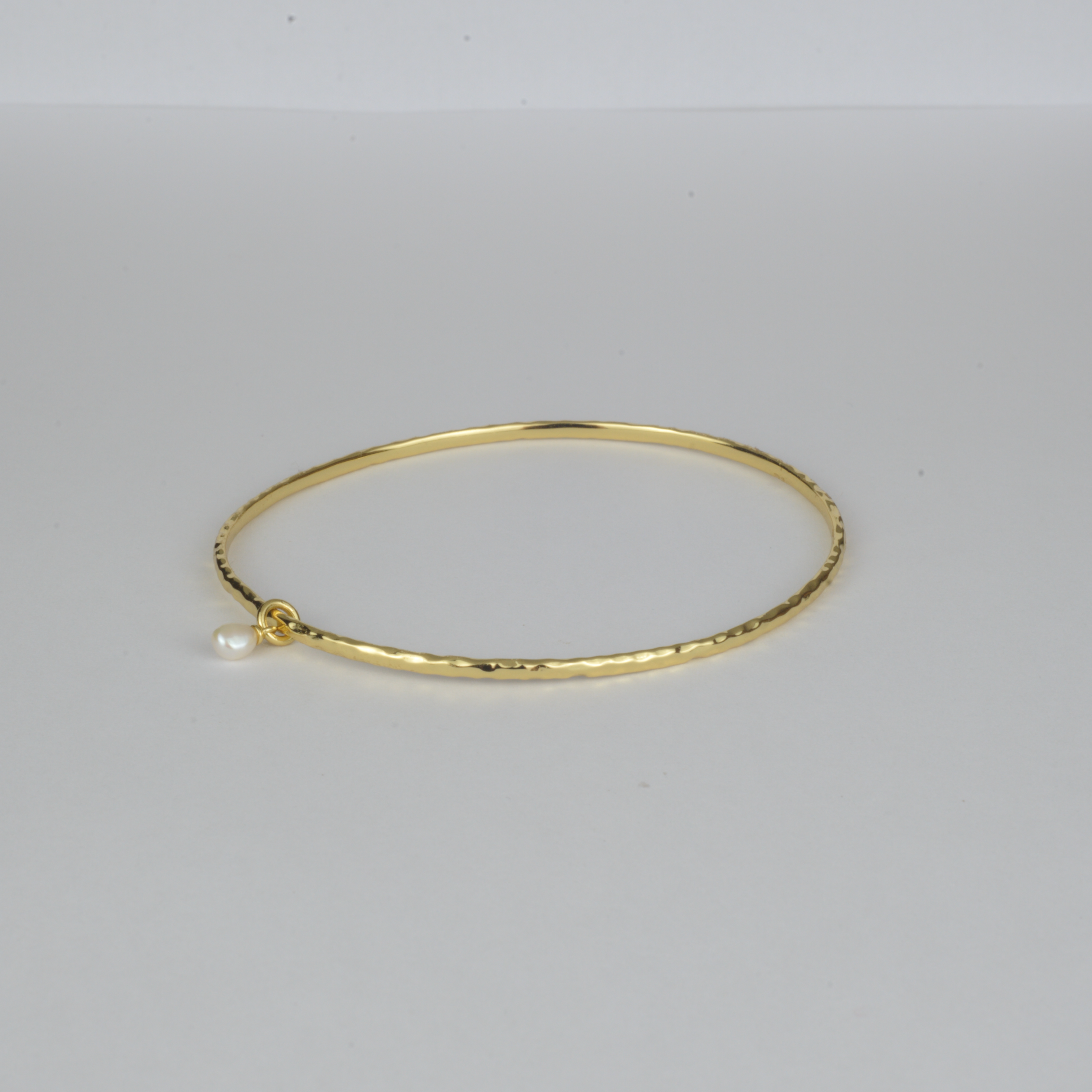 Nacre Bangle by Nudie – studio photo on white background showing the open bangle laid flat, featuring a petite freshwater pearl and hammered gold finish.